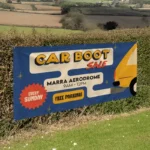6ft x 3ft PVC Banner: Printed car boot sale banner on a hedge by a field